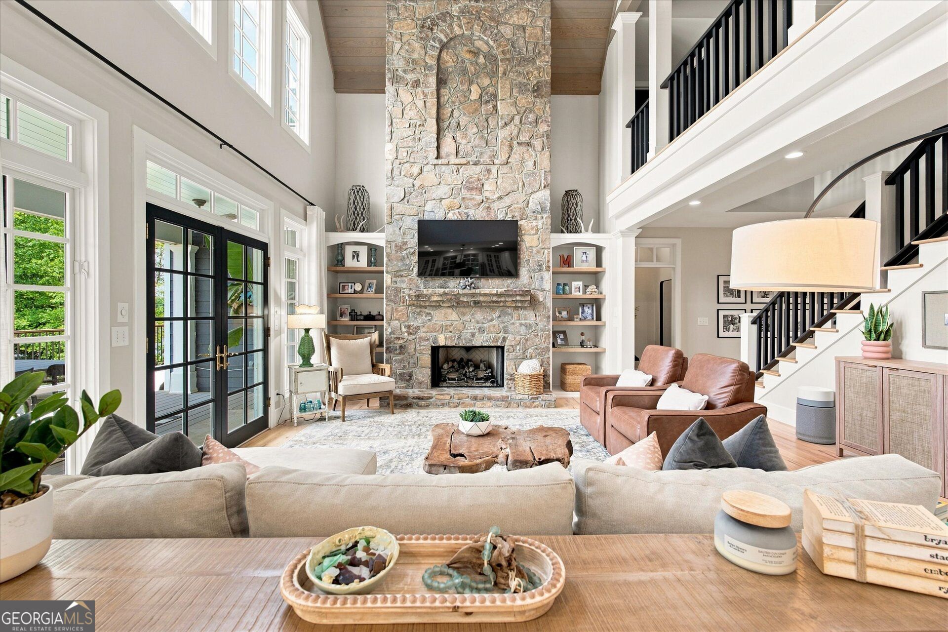Double-height living room with a towering stone fireplace, built-in shelves, and a black-railed staircase.