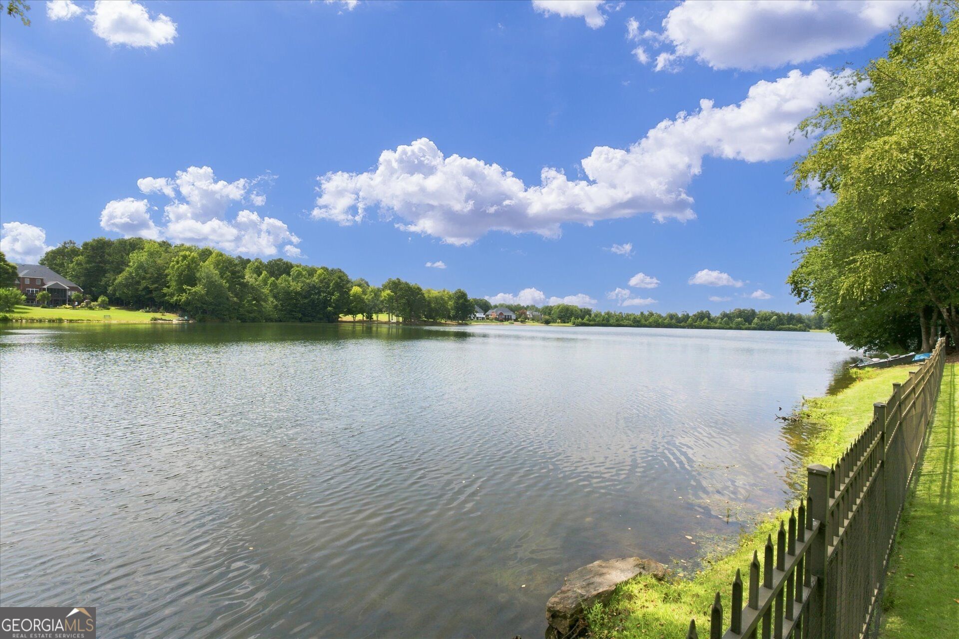 Neighborhood lake bordered by trees and homes, with a fenced grassy shoreline.
