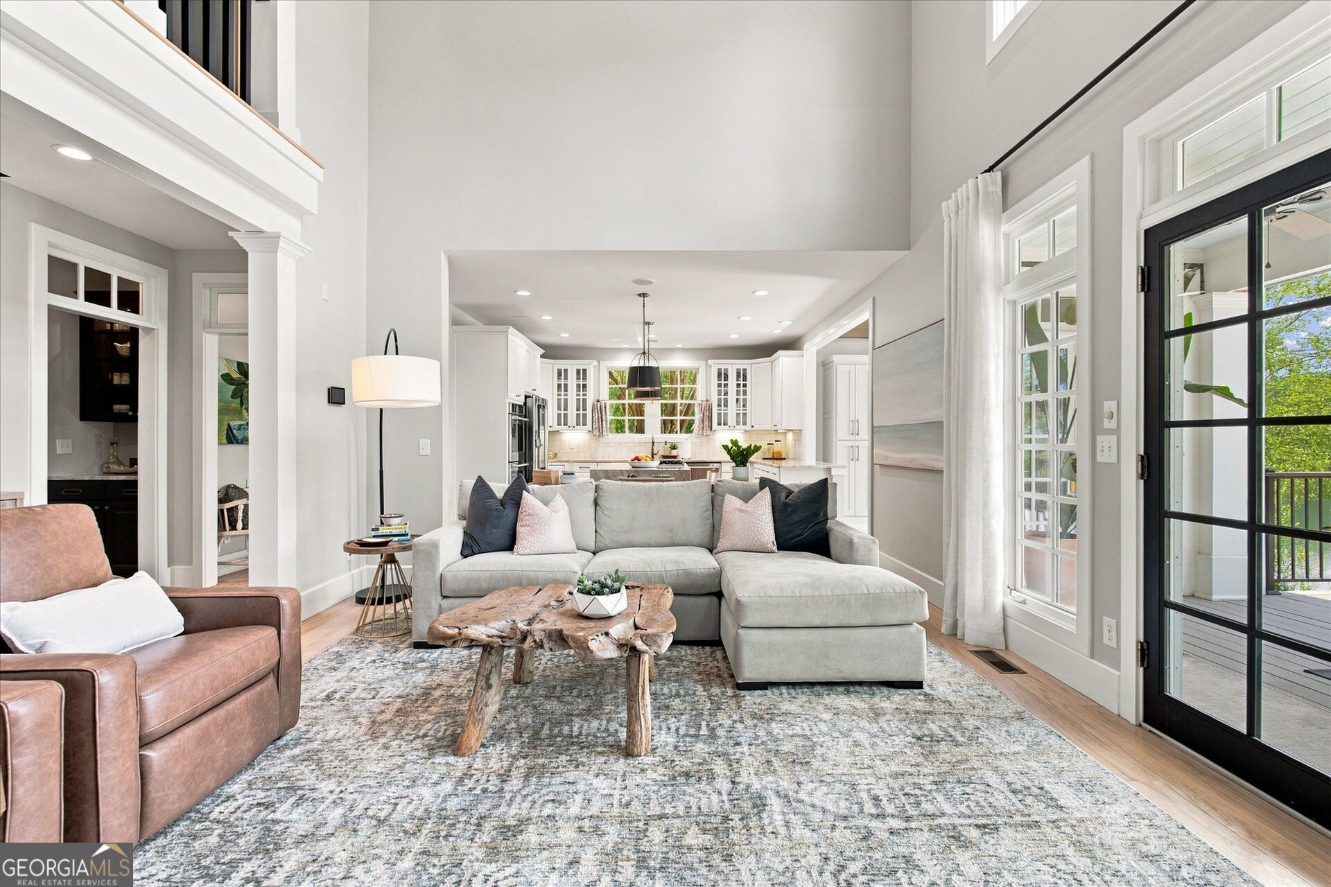 Living room with a gray sectional and rustic coffee table opening onto a white kitchen.