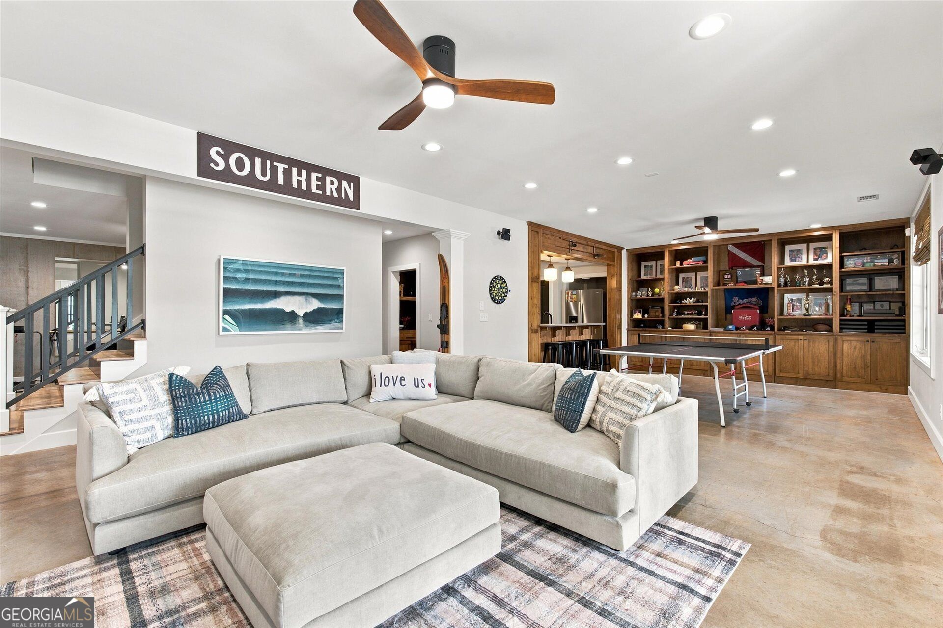 Furnished living room with a large sectional, built-in wood display cabinets, and a ping-pong table.