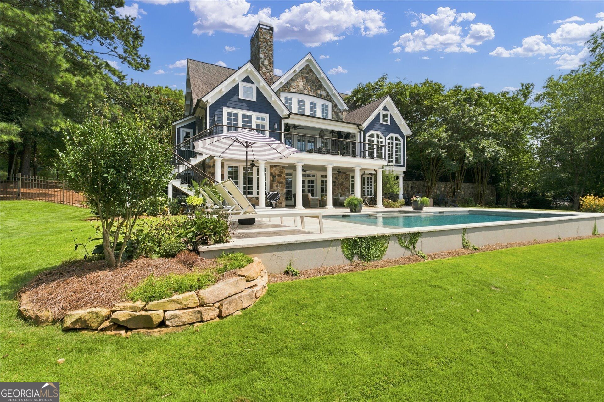 Blue-and-stone house with a covered patio and deck overlooking a backyard swimming pool.