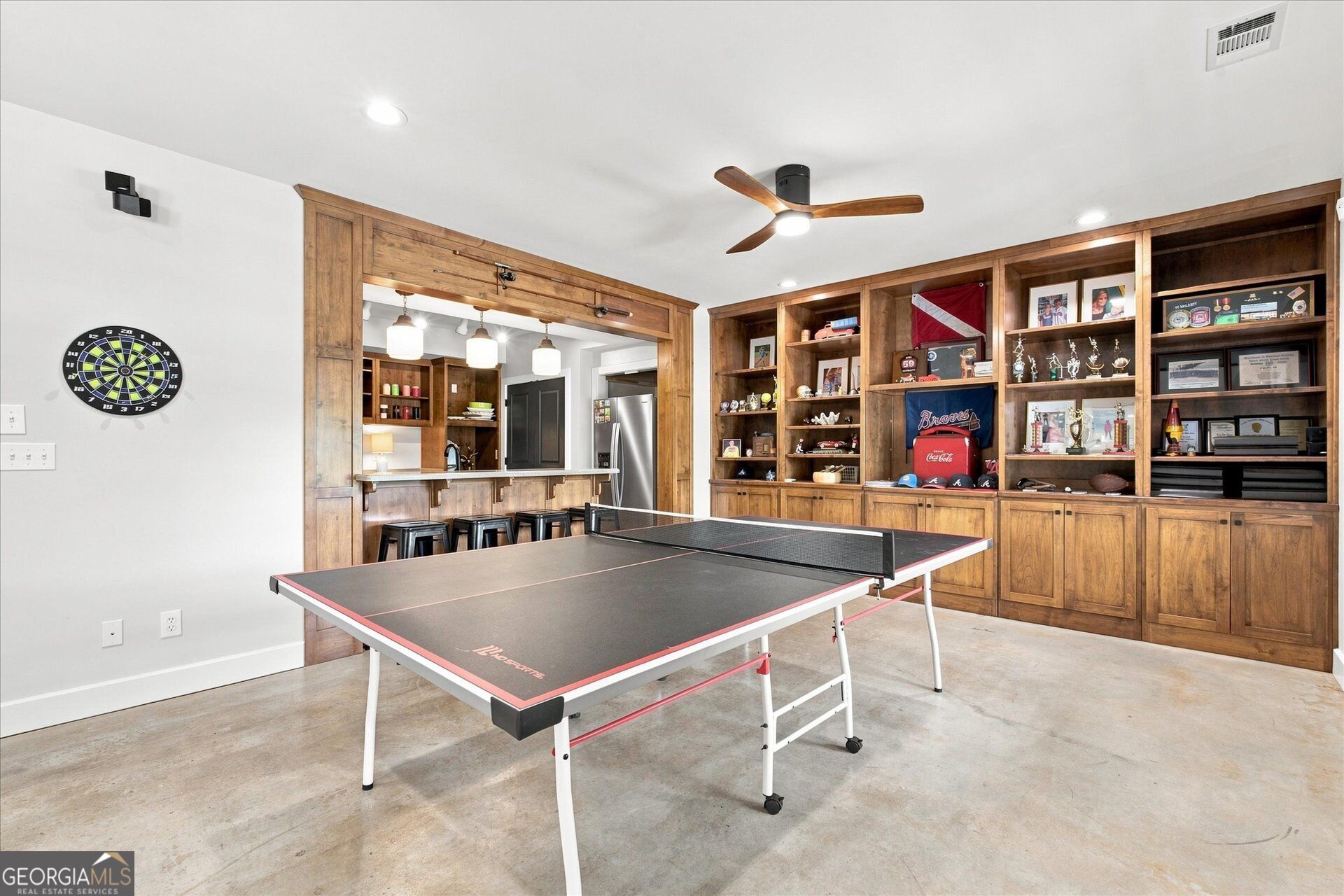 Game room with a ping-pong table, dartboard, and built-in wooden display shelves.