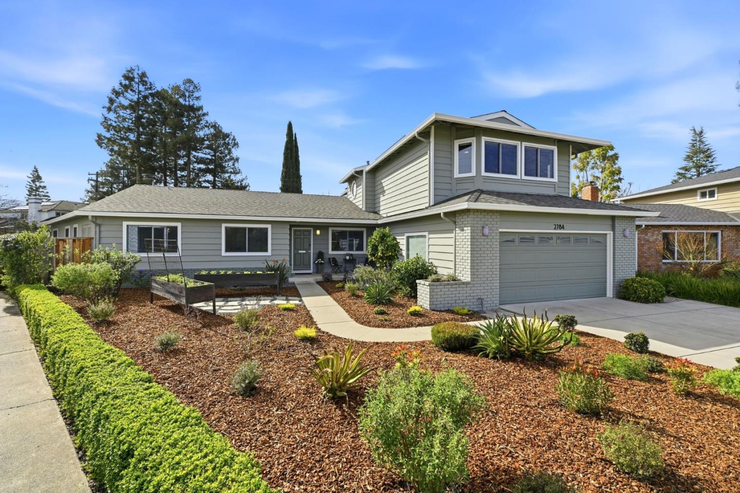 Two-story gray home with a white brick garage, landscaped front yard, and curved walkway.