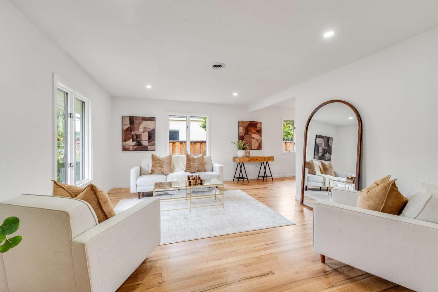 Staged living room with white sofas, warm hardwood floors, and a large arched mirror.