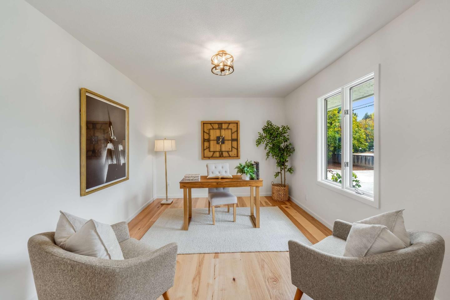Staged home office with a wooden desk, hardwood floors, and a large window overlooking greenery.