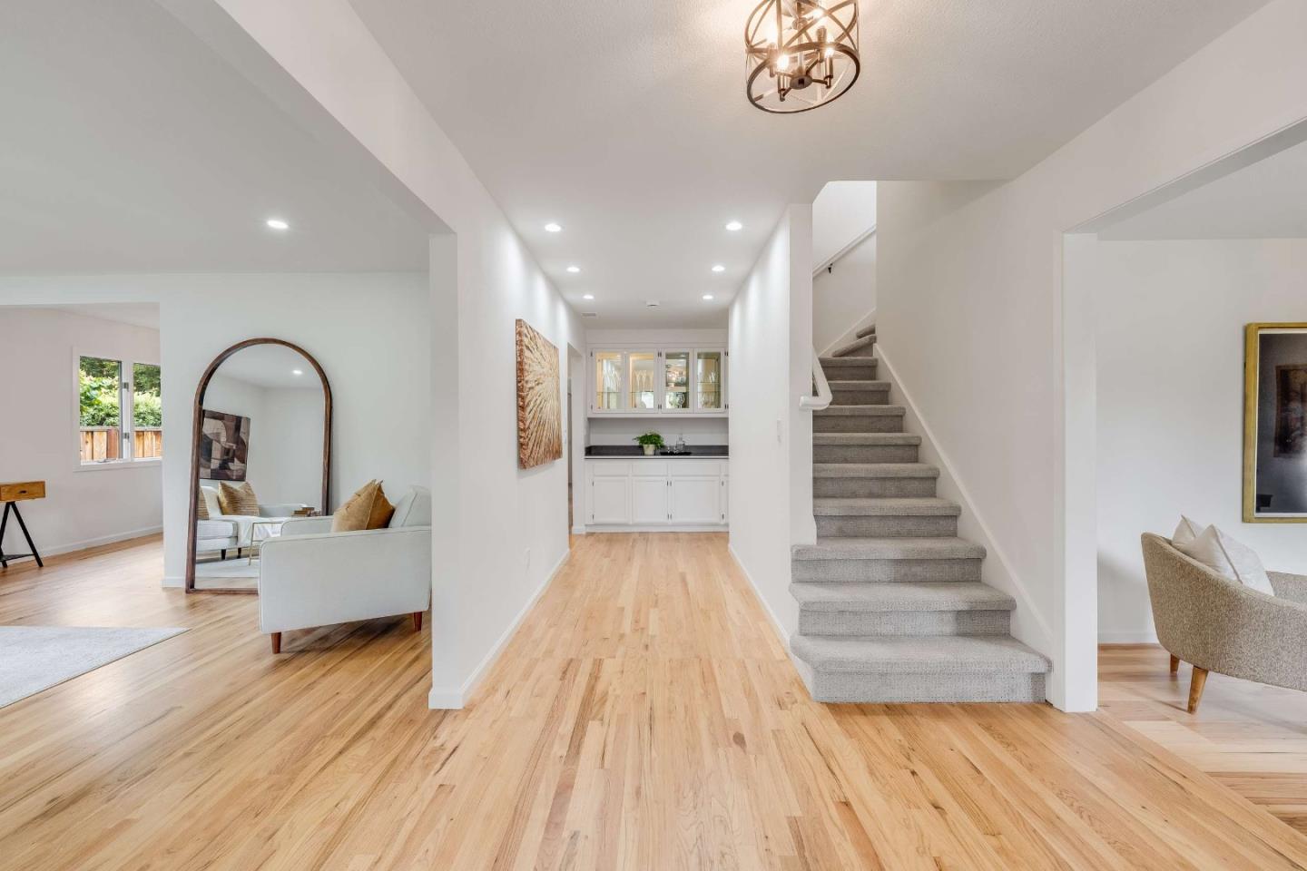 Bright entry hall with hardwood floors, carpeted staircase, and adjoining furnished sitting areas.