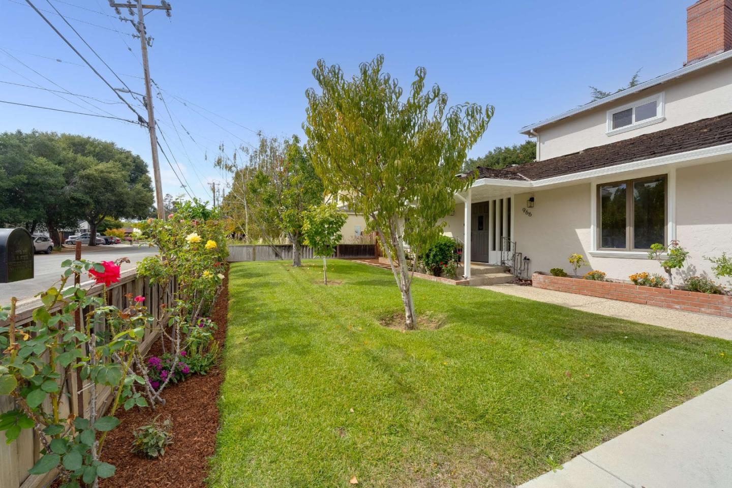 Home exterior with a broad lawn, covered entry, and rose bushes along the fence.