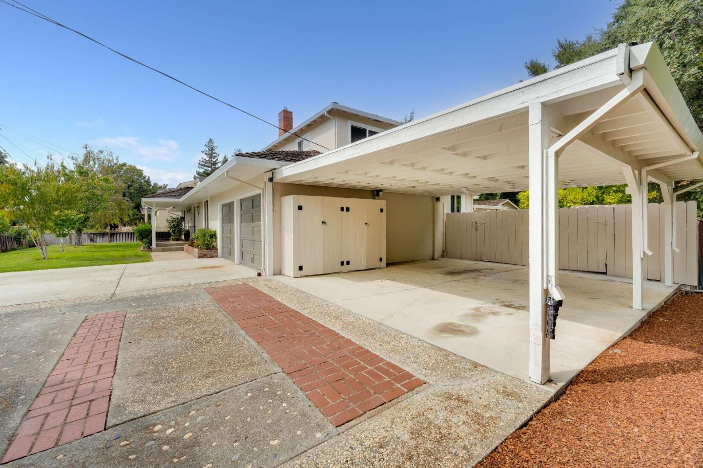 Covered carport beside the house, with garage doors and brick-and-concrete paving.