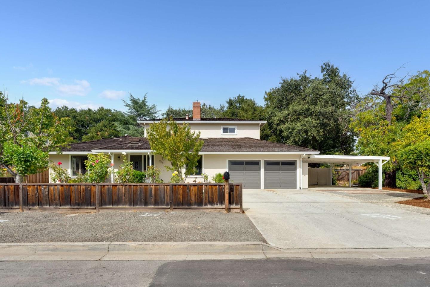 Two-story home with gray garage doors, a covered carport, and a wooden front fence.