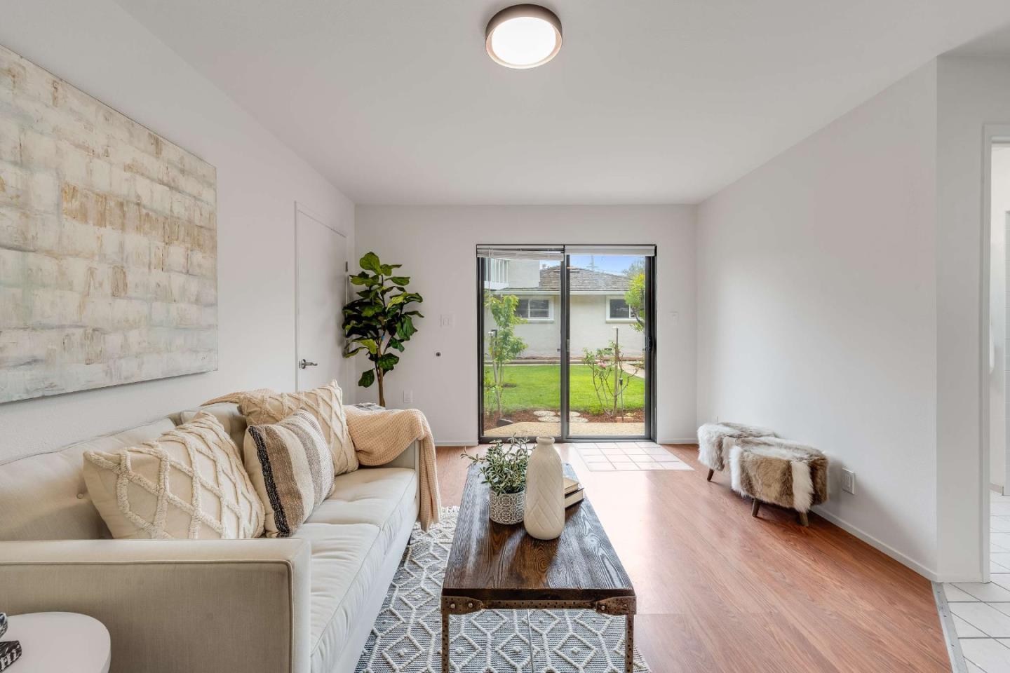 Staged living room with a cream sofa and sliding glass doors overlooking a garden lawn.