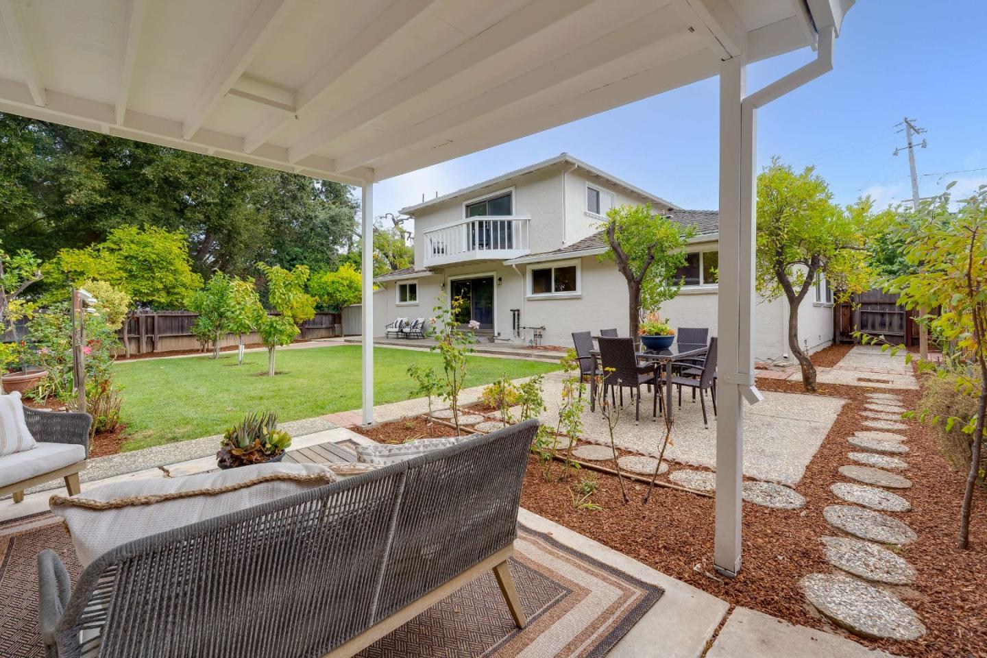 Covered backyard patio with outdoor seating, lawn, and a two-story home.