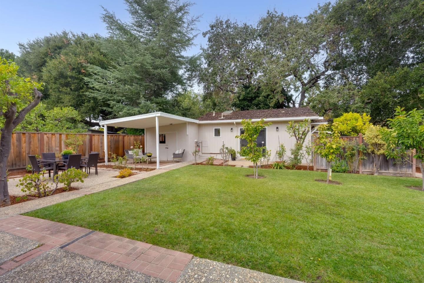 Single-story home's rear yard with covered patio, dining set, and broad green lawn.