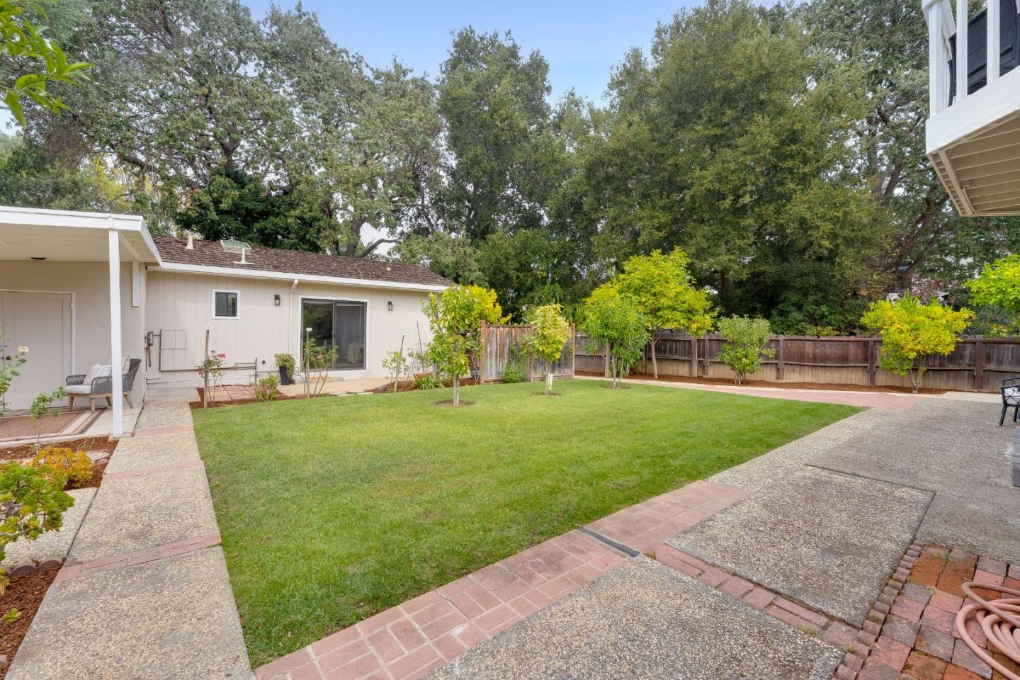 Backyard with a broad lawn, paved patio, wooden fencing, and mature trees.