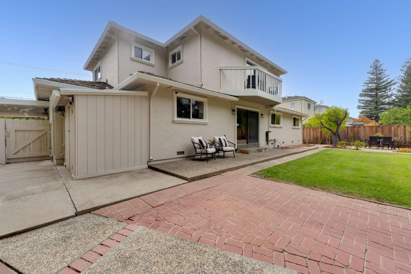 Two-story home's rear exterior with a balcony, brick patio, lawn, and outdoor seating.