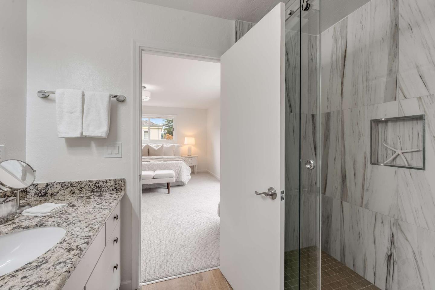 Bathroom with a granite vanity and marble-look tiled shower, opening onto a bedroom.