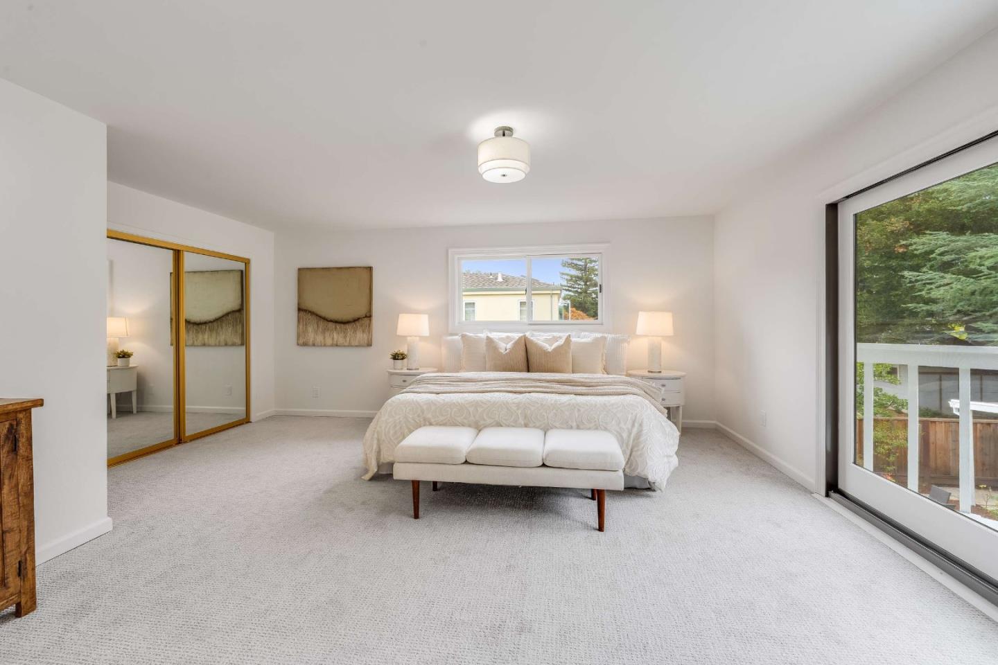 Bright bedroom with a king-size bed, mirrored closet doors, and sliding glass doors to a tree-lined deck.