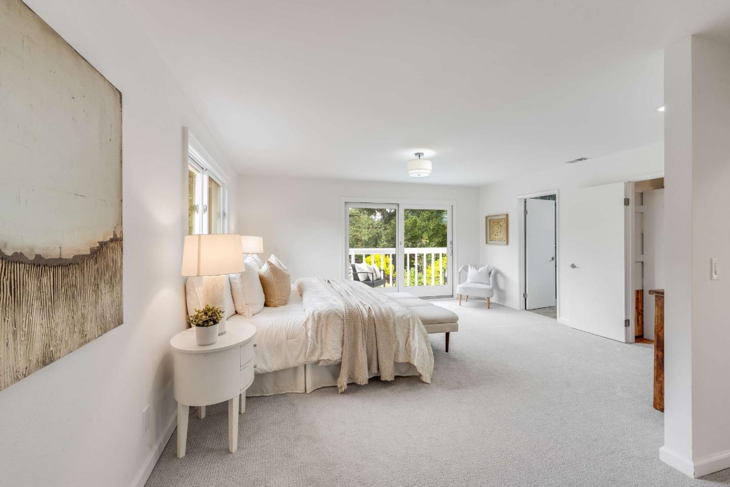 Bright bedroom with a white bed and sliding glass doors overlooking greenery.