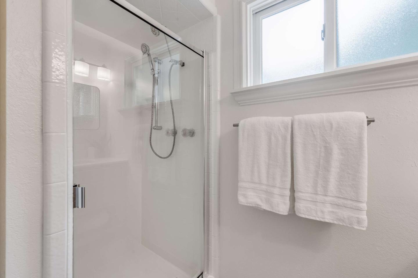 White bathroom shower with glass enclosure, frosted window, and two towels.
