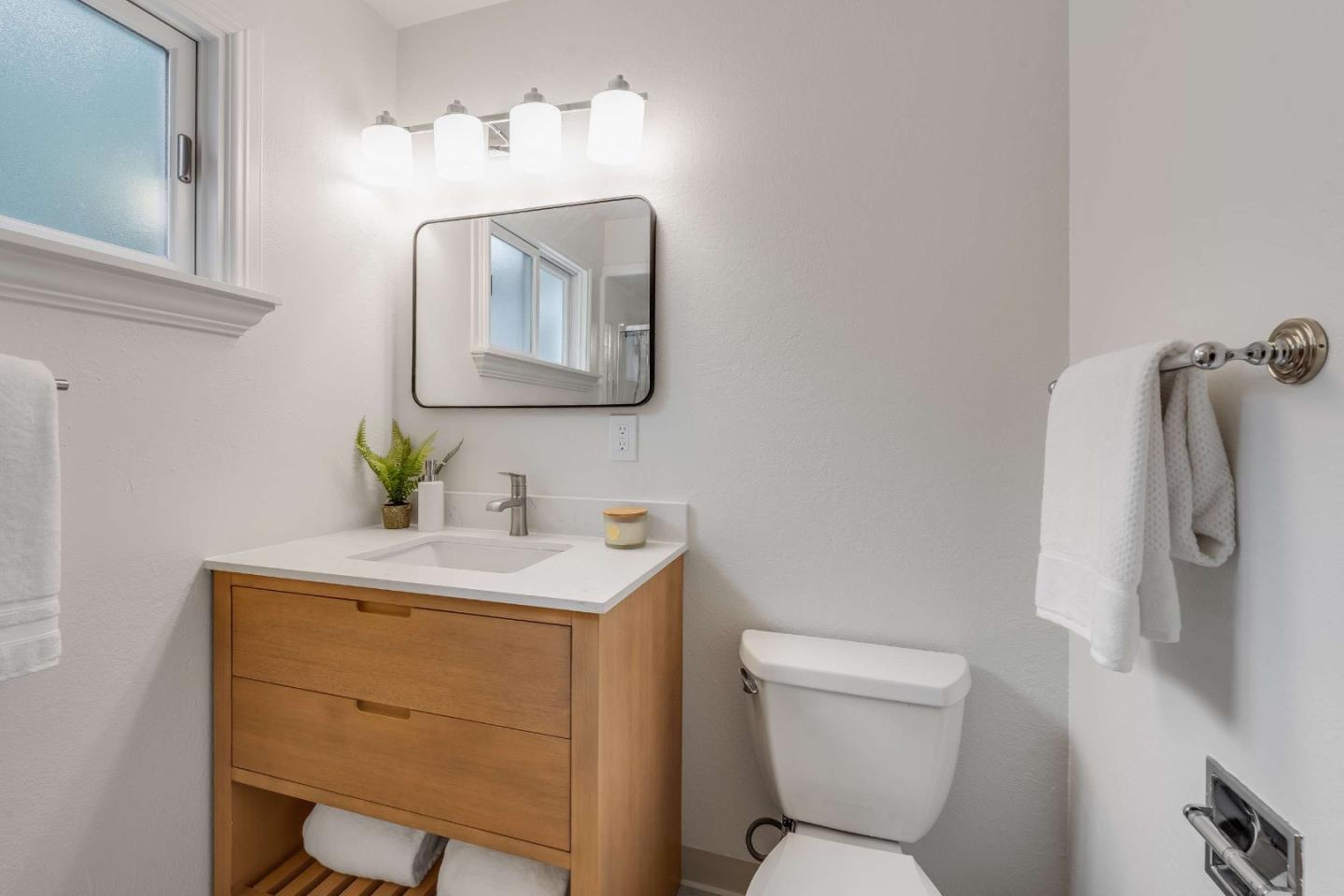 Bathroom with a wood vanity, white sink, mirror, toilet, and frosted window.