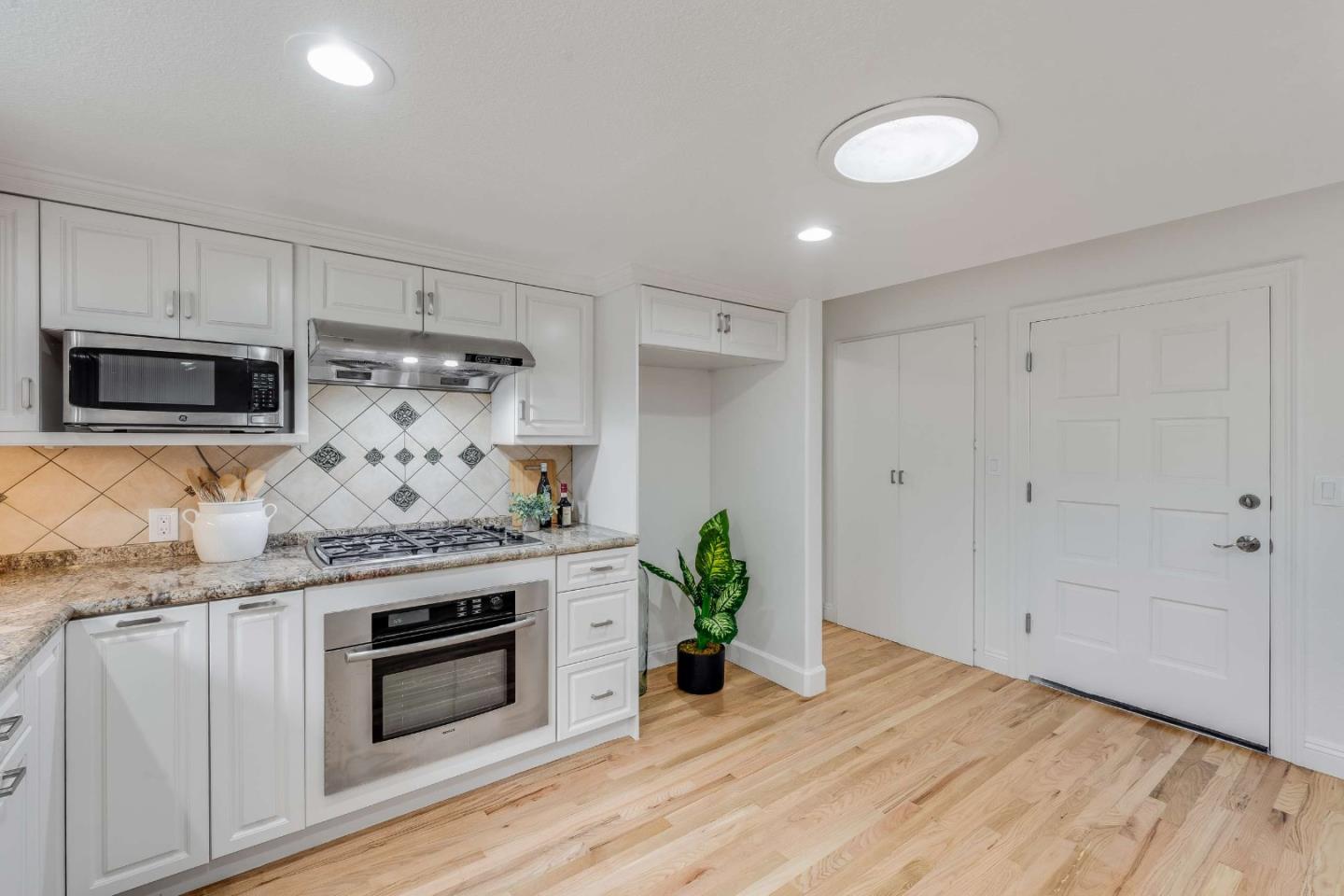 Kitchen with white cabinets, stainless appliances, patterned tile backsplash, and light hardwood floors.