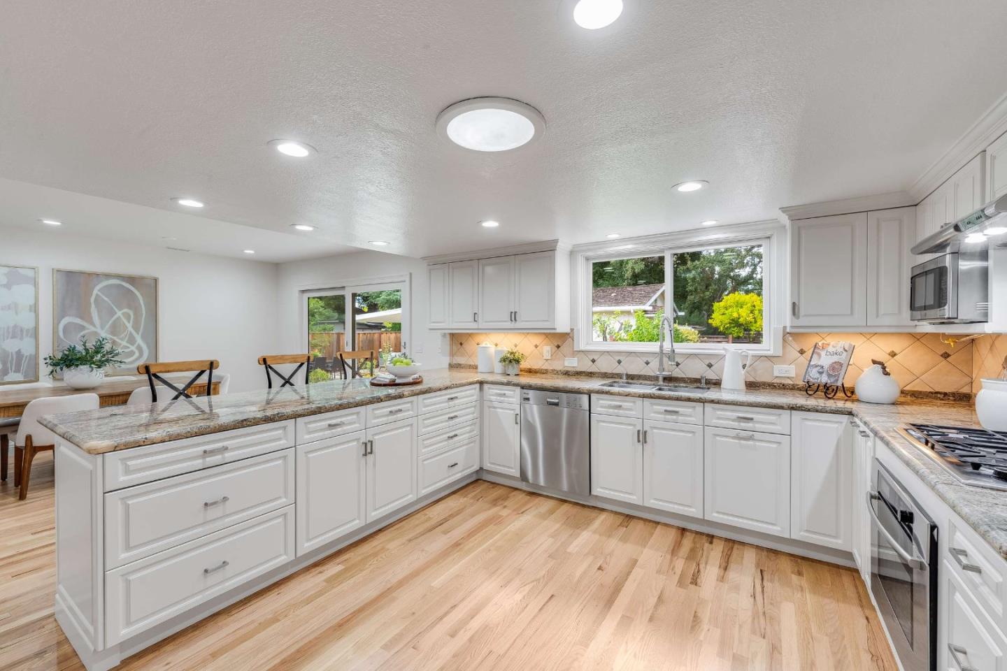 Bright white kitchen with granite counters, stainless appliances, hardwood floors, and a garden view.
