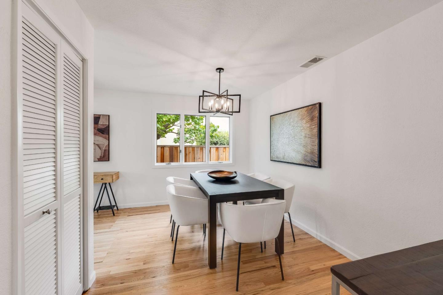 Dining room with a dark table, white chairs, geometric pendant, and window overlooking a fenced yard.
