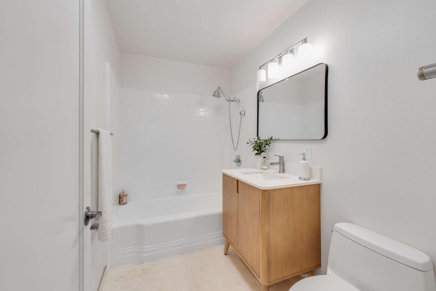 Bathroom with a white tub and shower, light wood vanity, large mirror, and toilet.