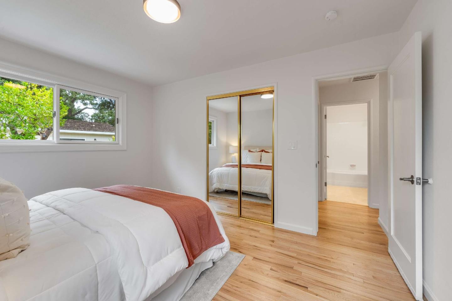 Staged bedroom with a white bed, rust-colored throw, mirrored closet doors, and hardwood floors.