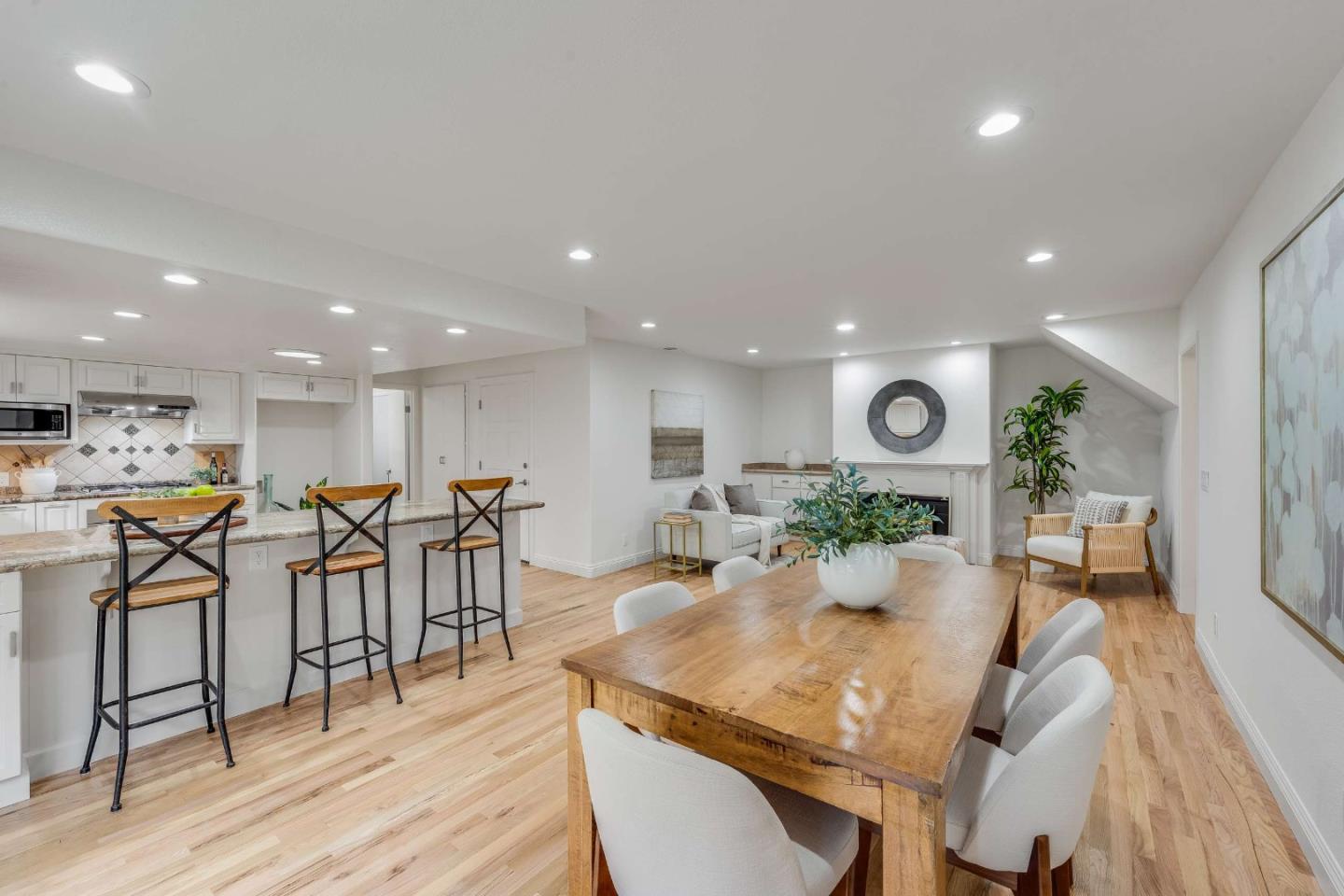 Open-plan kitchen and dining area with a stone island, wood table, and adjoining fireplace seating area.