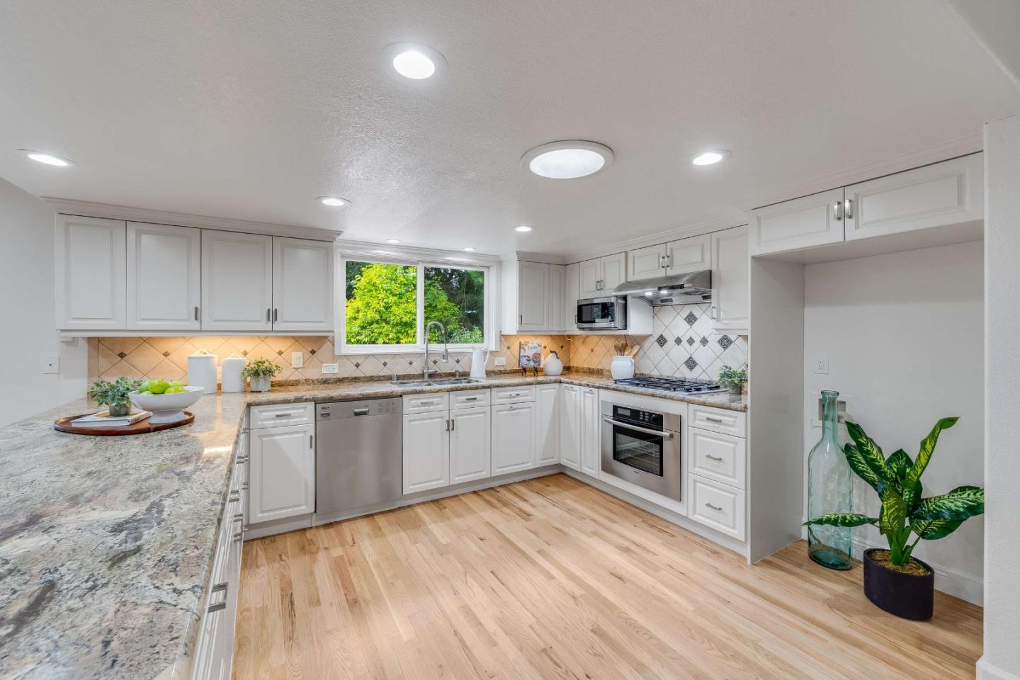 Bright kitchen with white cabinets, granite counters, stainless steel appliances, and light wood floors.