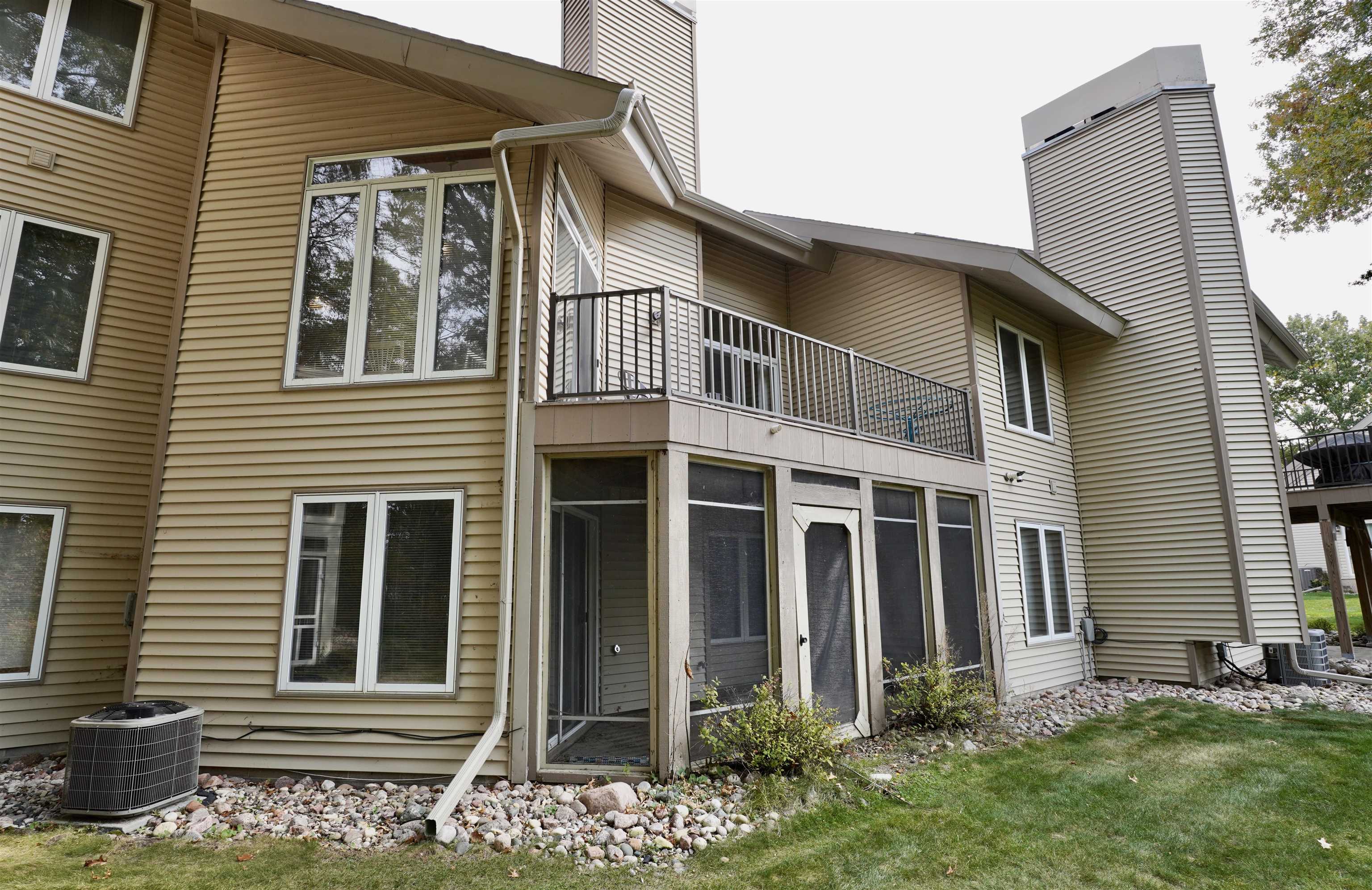 Home’s rear exterior with a raised deck, screened patio, tall chimney, and rock landscaping.