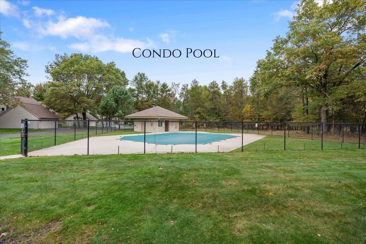 Fenced condo pool with a broad concrete deck and wooded surroundings.