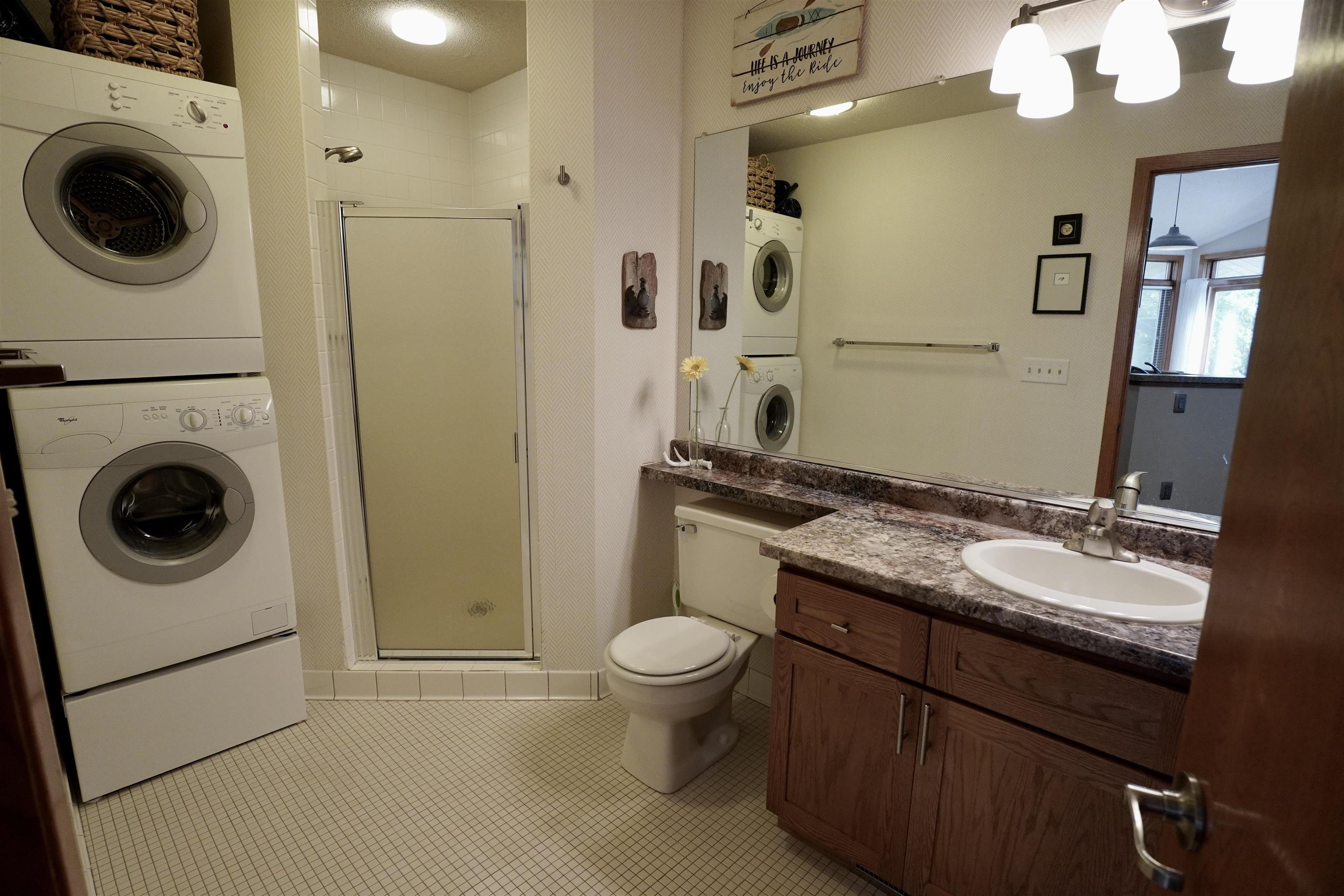 Bathroom with a stacked washer and dryer beside the shower and a wood vanity.