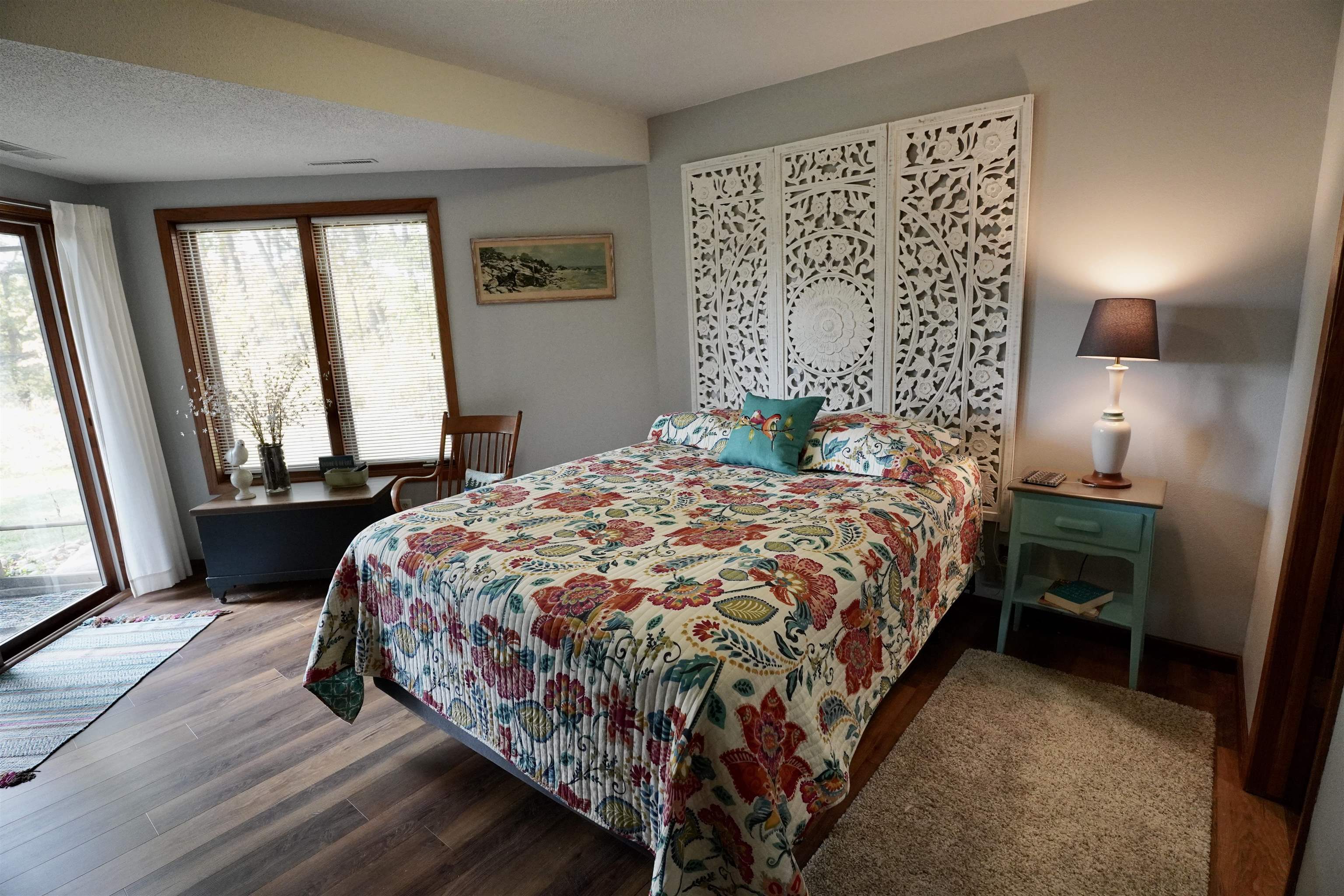 Bedroom with colorful floral bedding, an ornate white screen, and a sliding glass door.