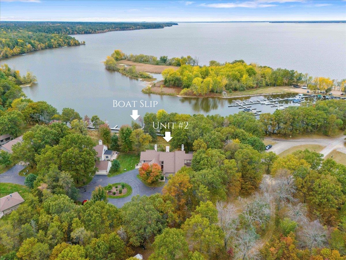 Aerial view of Unit #2 beside a wooded lake, boat slip, and marina.