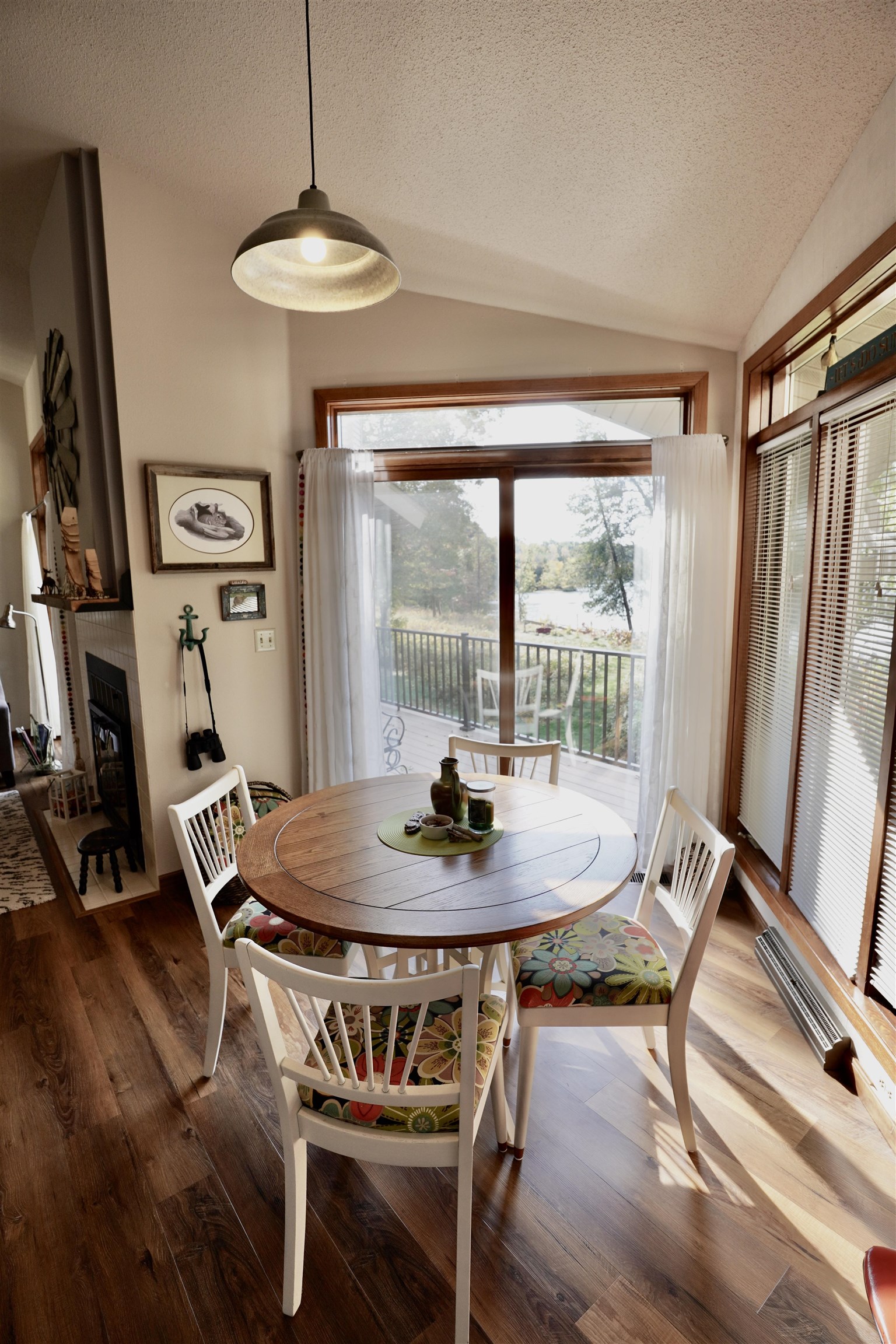 Dining area with a round wooden table and colorful chair cushions overlooking a deck and lake.