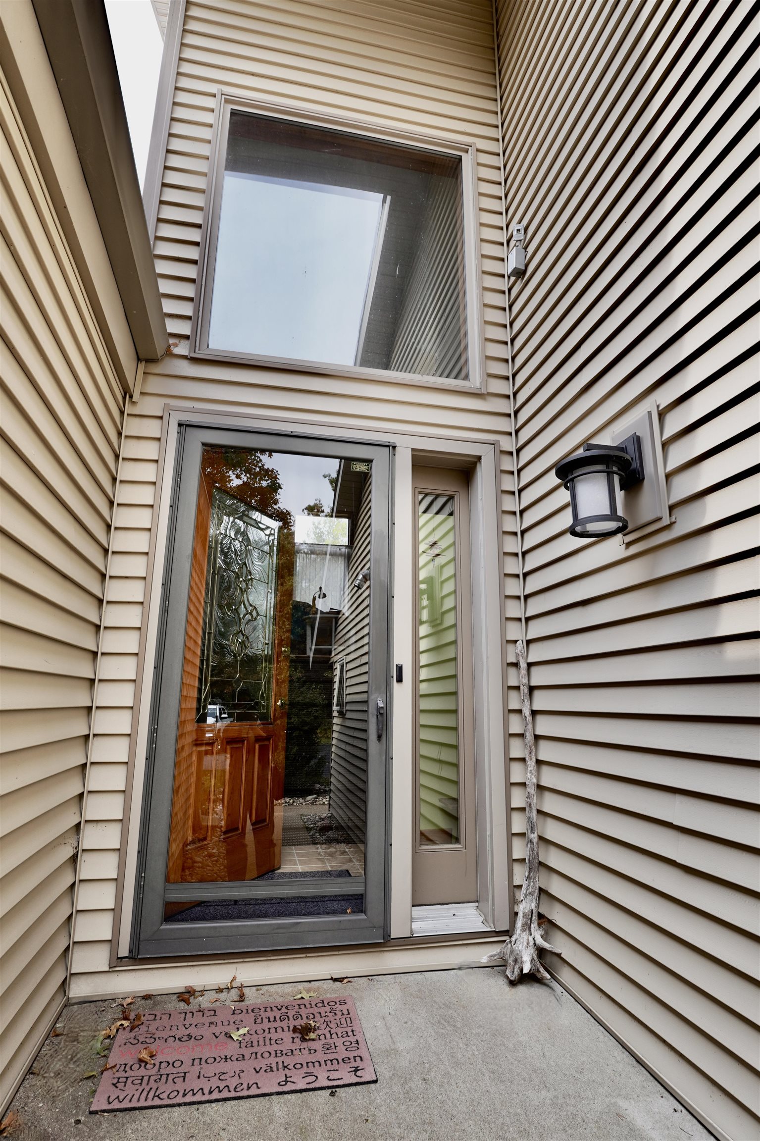 Home entry with a glass storm door, decorative wooden door, exterior lantern, and multilingual welcome mat.