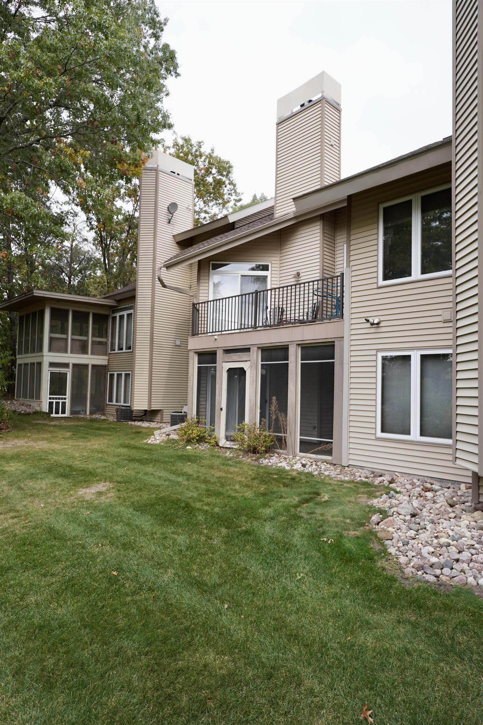 Beige residence with a raised balcony, screened porch, and broad lawn.