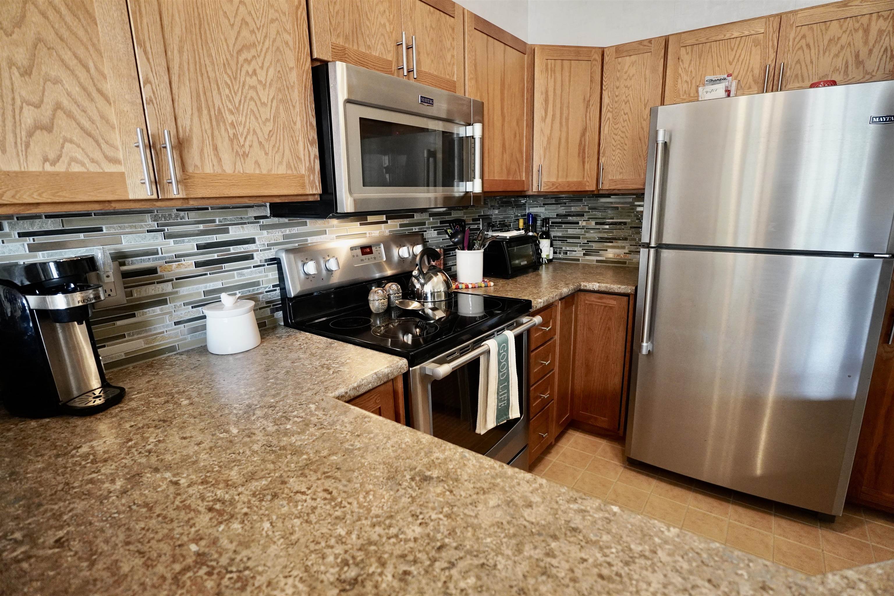 Kitchen with wood cabinets, a multicolored tile backsplash, and stainless steel appliances.