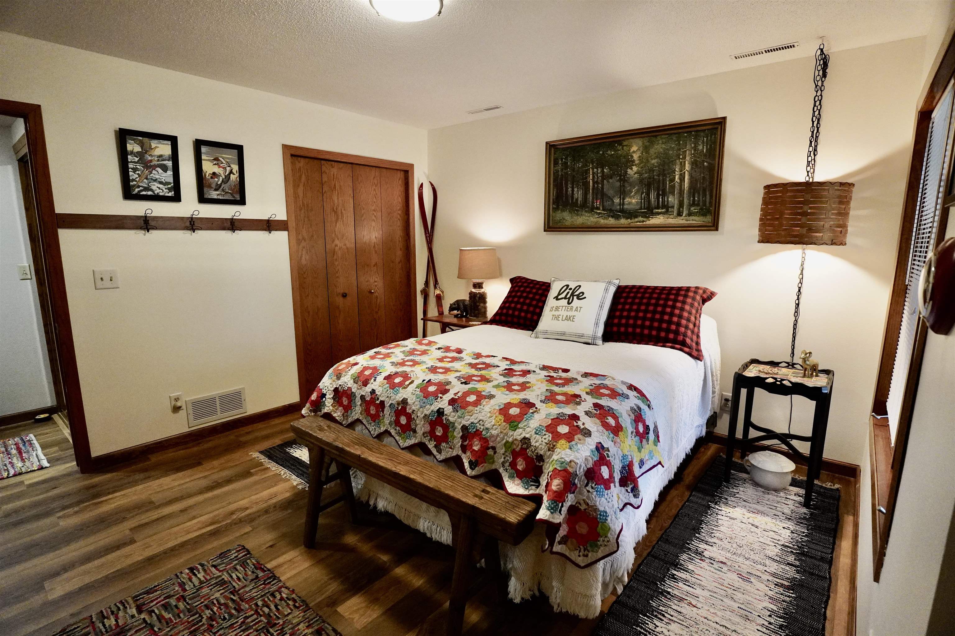 Bedroom with a colorful patchwork quilt, plaid pillows, and a wooden bench at the foot of the bed.