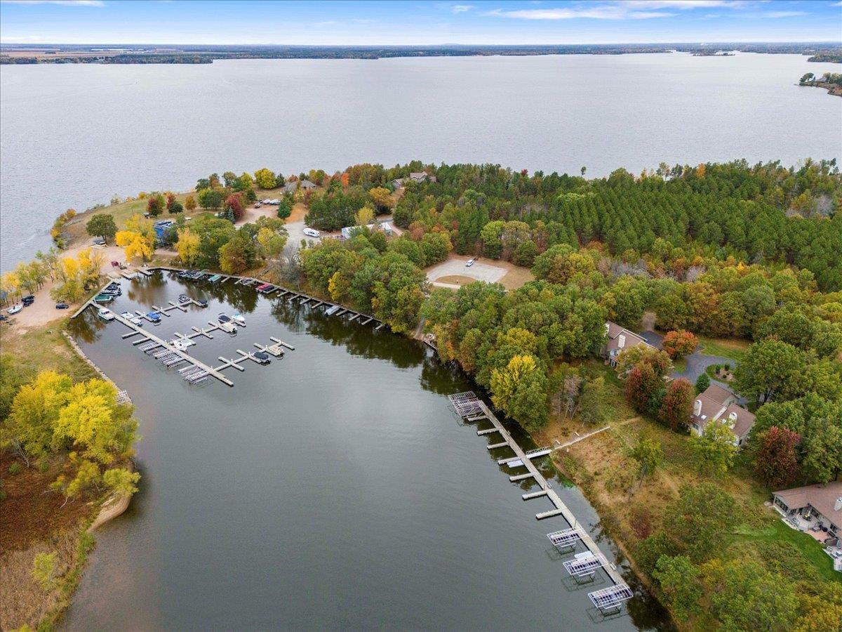Aerial view of a lakeside marina with boat slips, wooded shoreline, and nearby homes.
