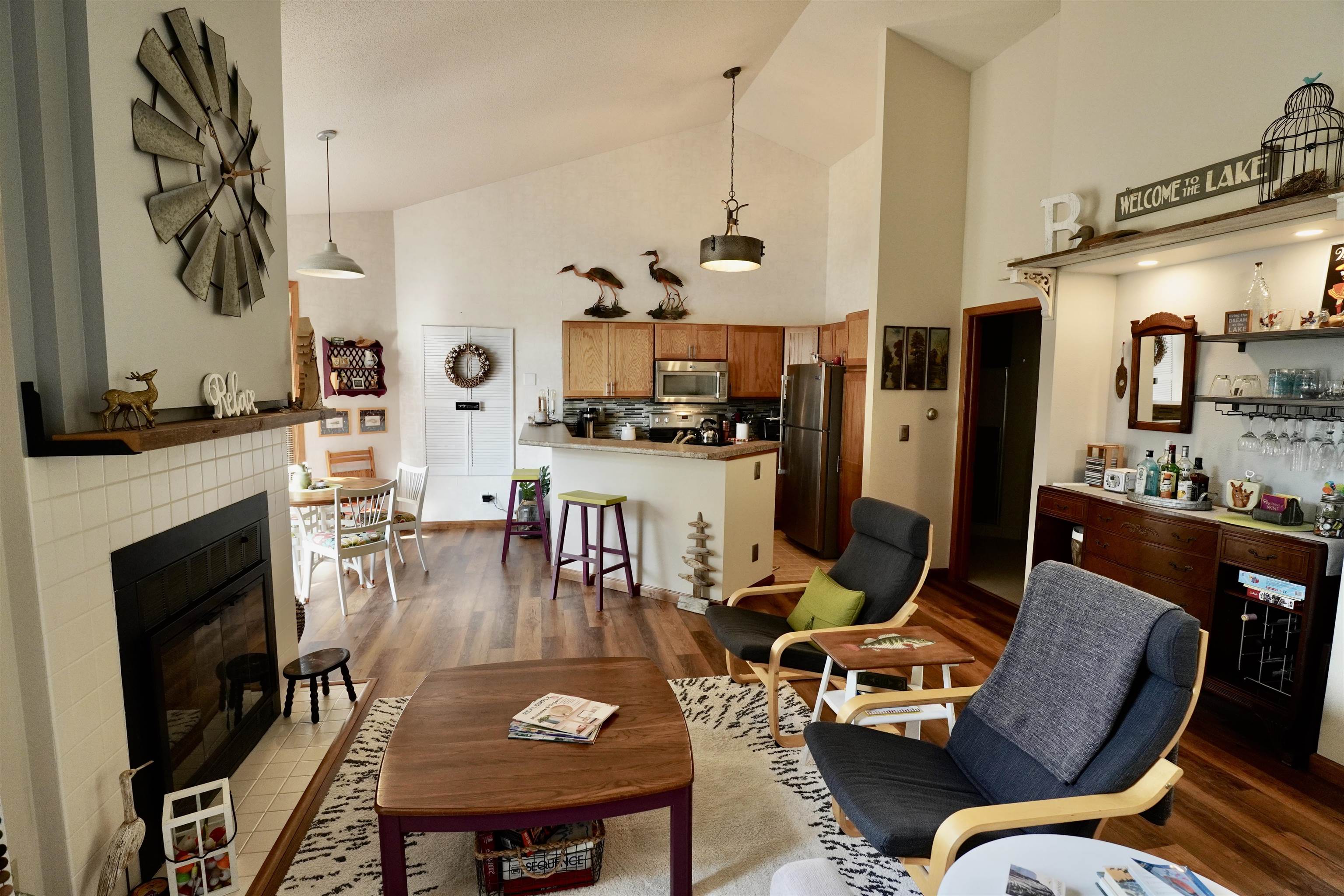 Open-plan living room and kitchen with a tiled fireplace, wood cabinets, and lake-themed décor.
