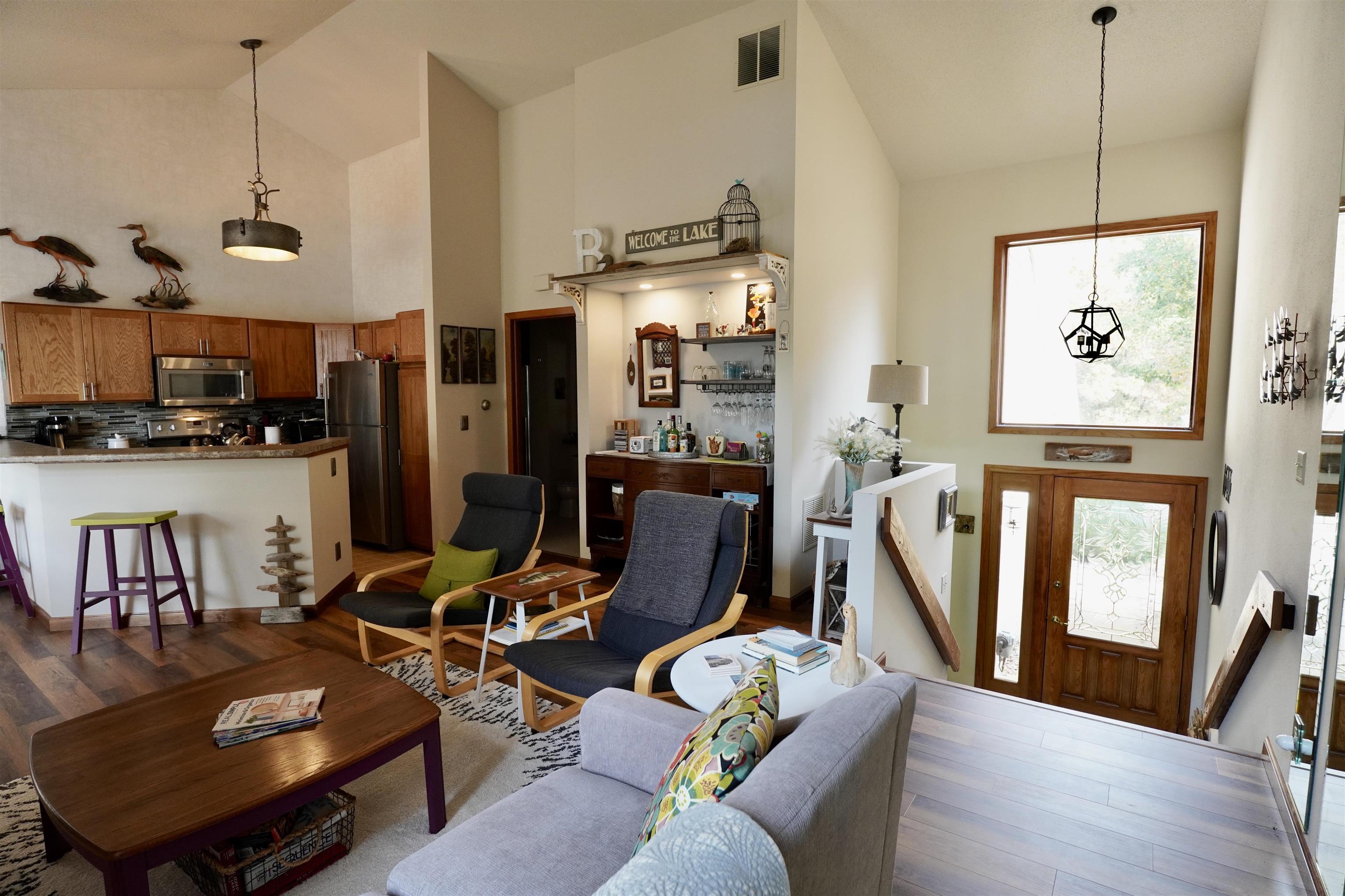 Open-plan living room and kitchen with vaulted ceilings, wood cabinetry, and a built-in bar.