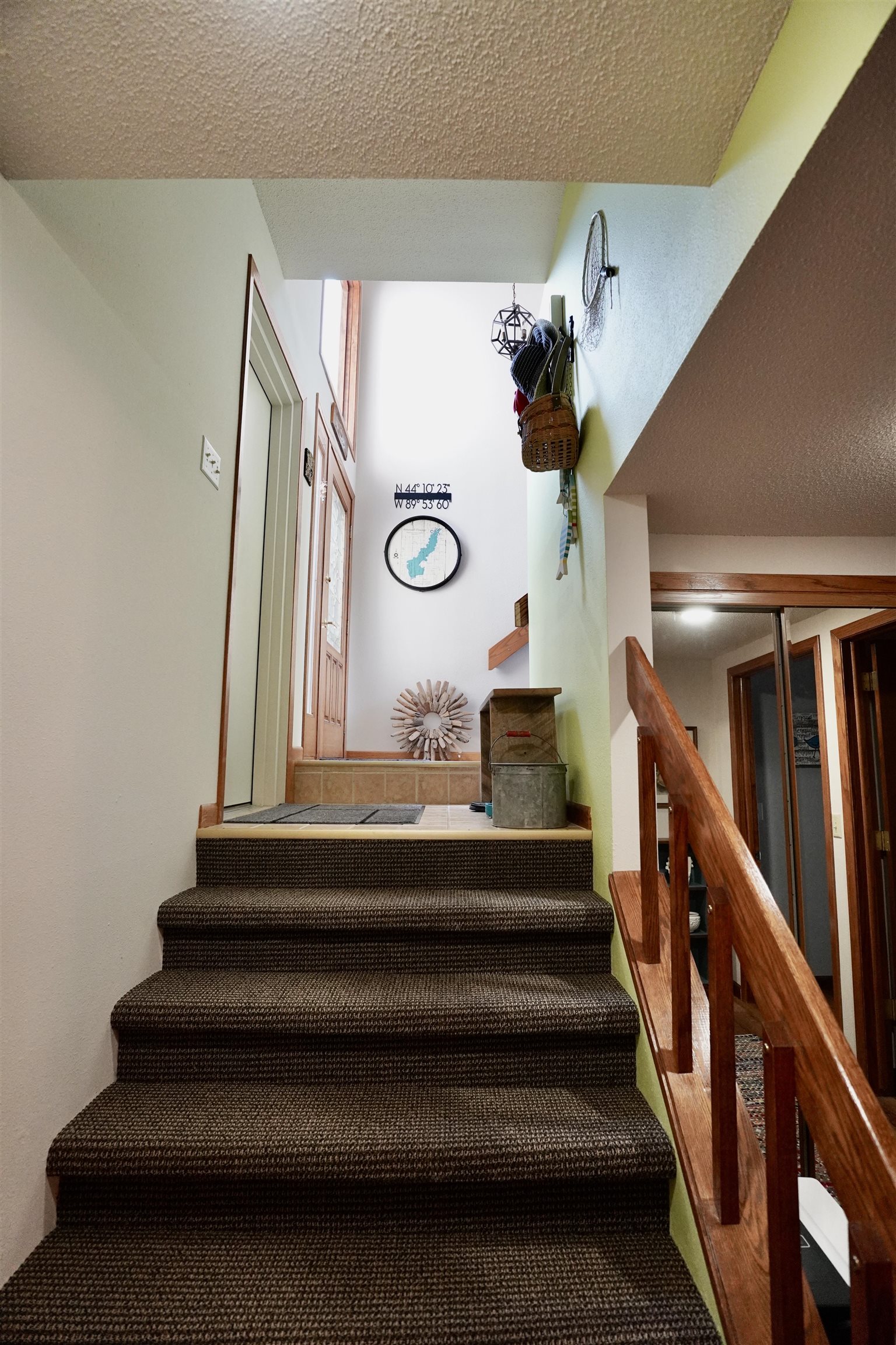 Carpeted staircase with a polished wood railing leading to a tiled entry landing.