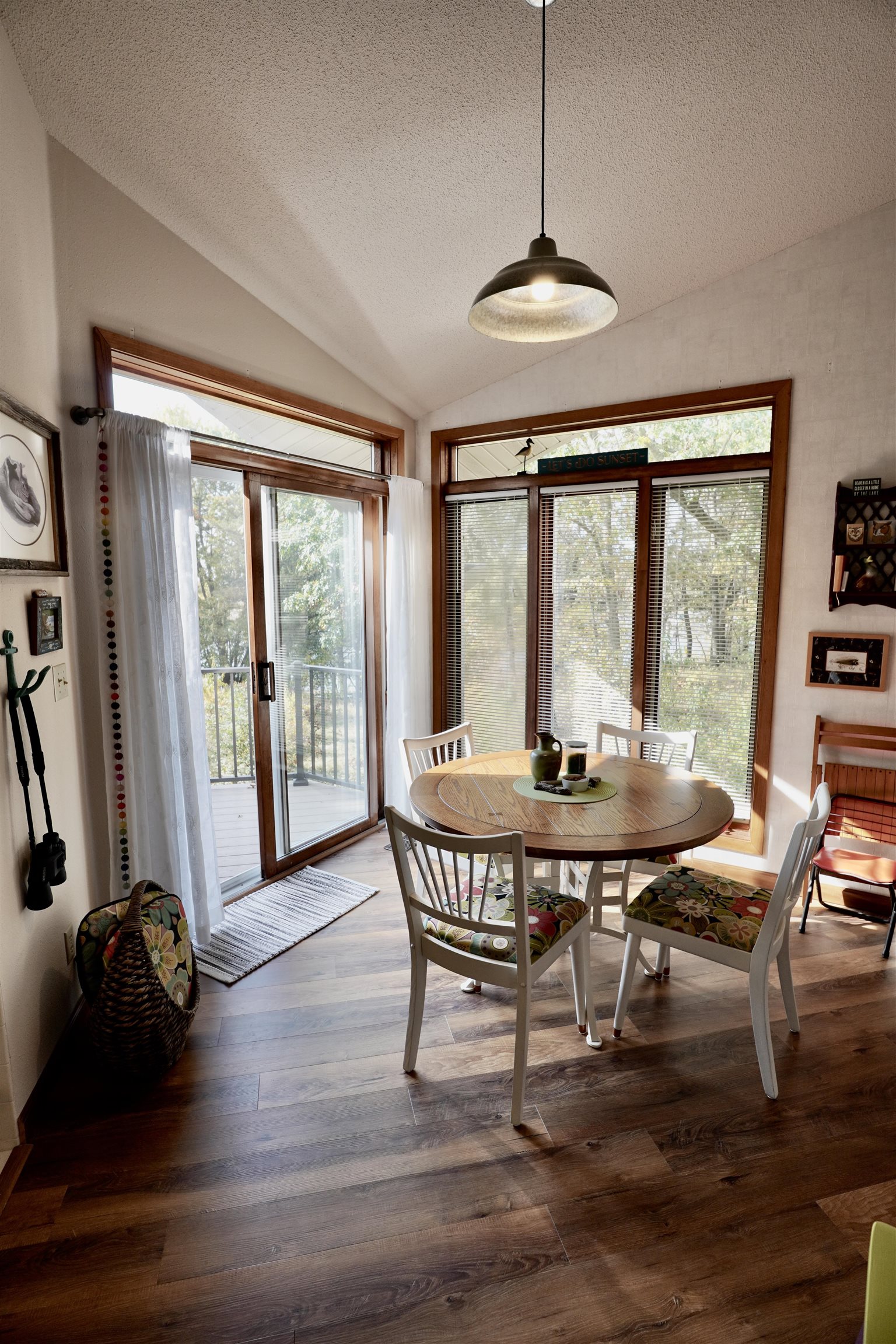 Dining room with a round wooden table, floral chair cushions, vaulted ceiling, and large windows.