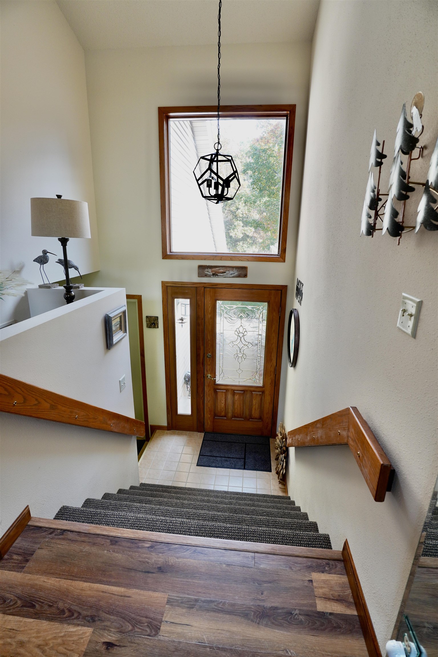 Foyer staircase leading to a wood front door with decorative glass and a large window above.