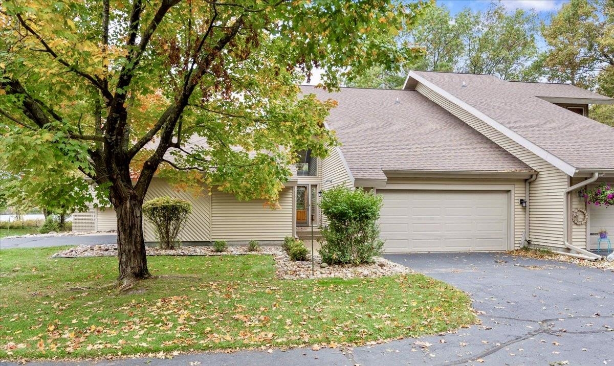 Beige-sided home with an attached two-car garage, driveway, and autumn trees.