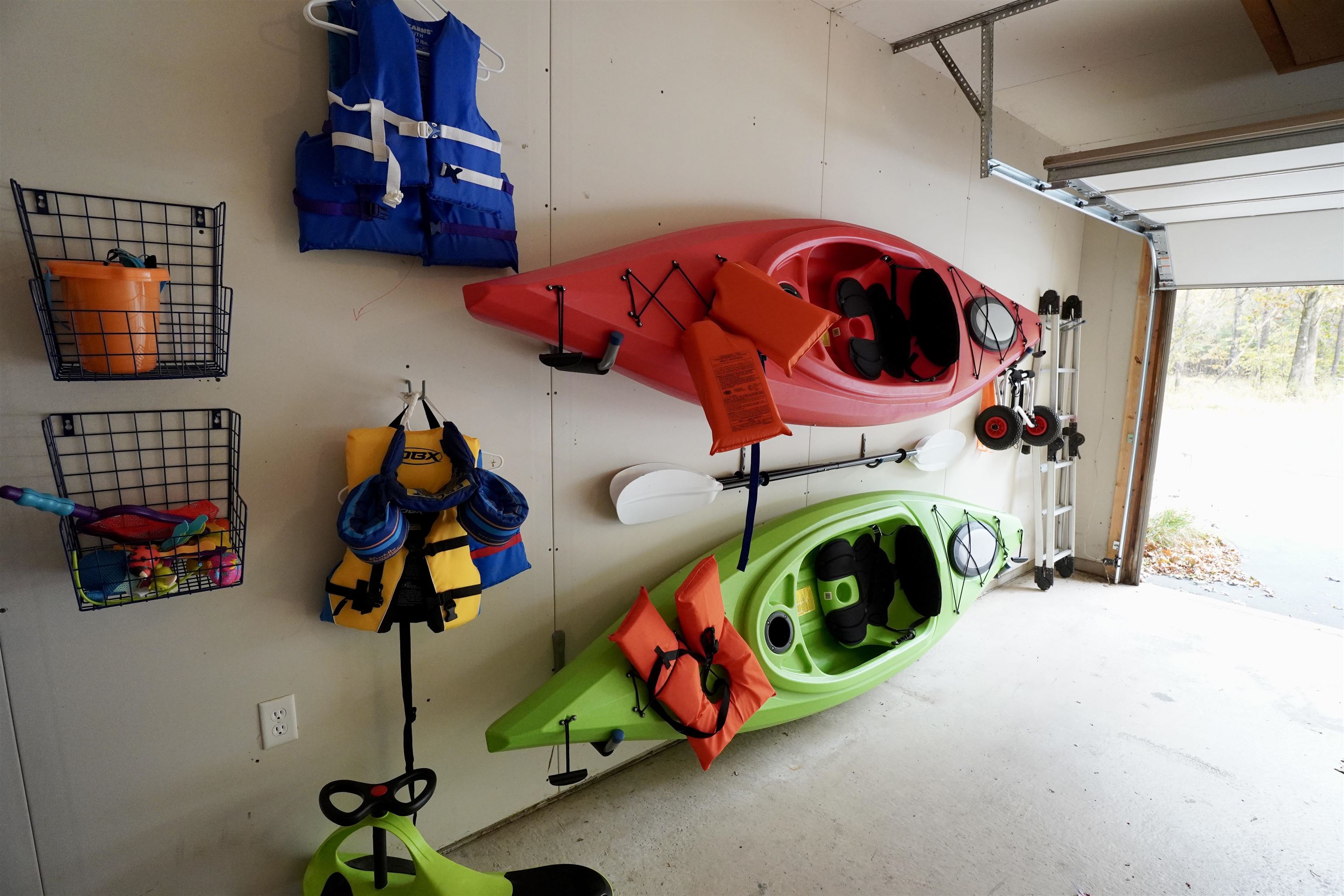 Garage with wall-mounted kayaks, life jackets, paddles, and an open garage door.
