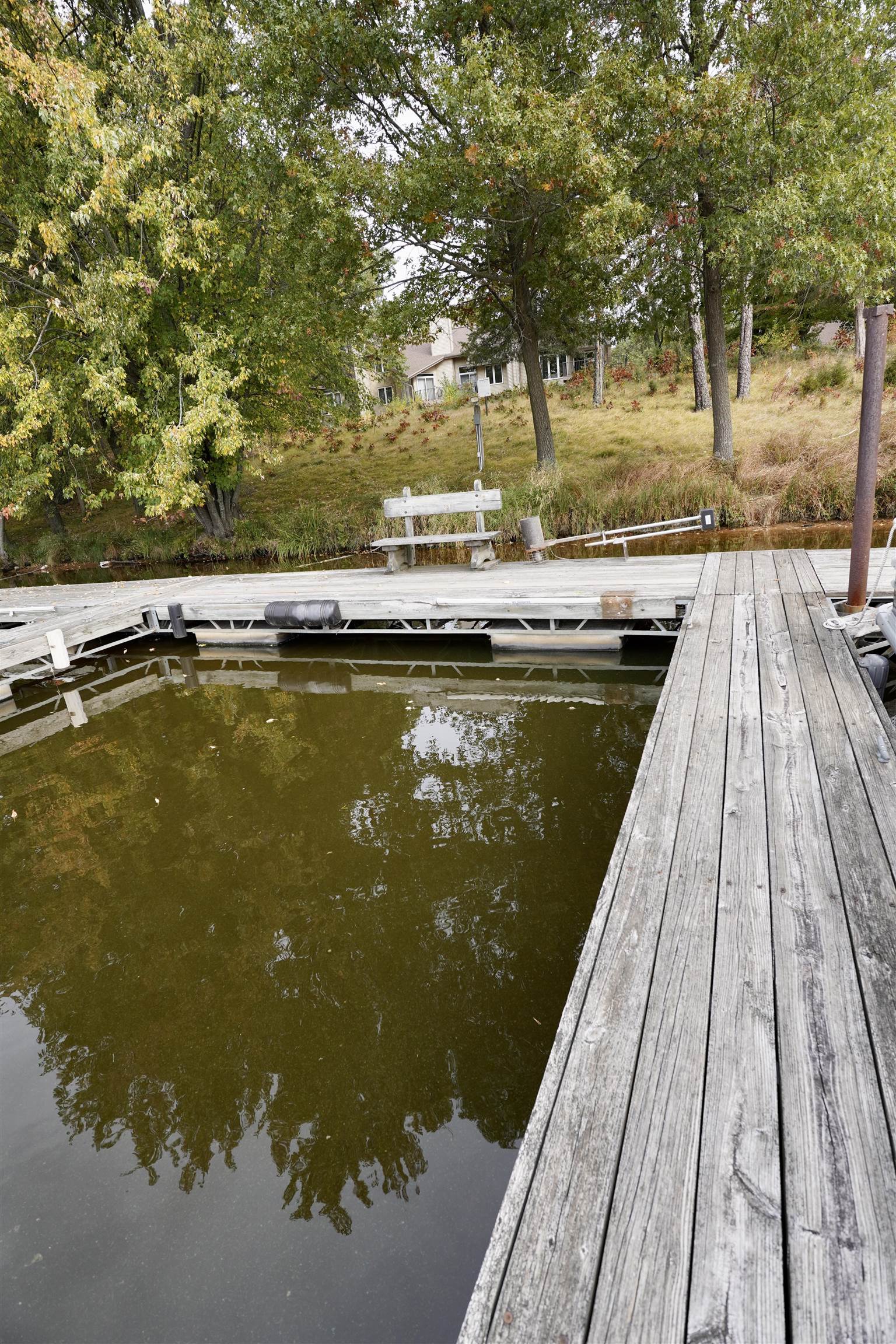 Wooden dock over calm water, with a bench and autumn trees along the bank.