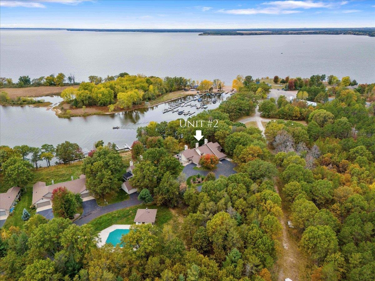 Aerial view of Unit 2 among wooded lakeside homes, with a marina and pool nearby.